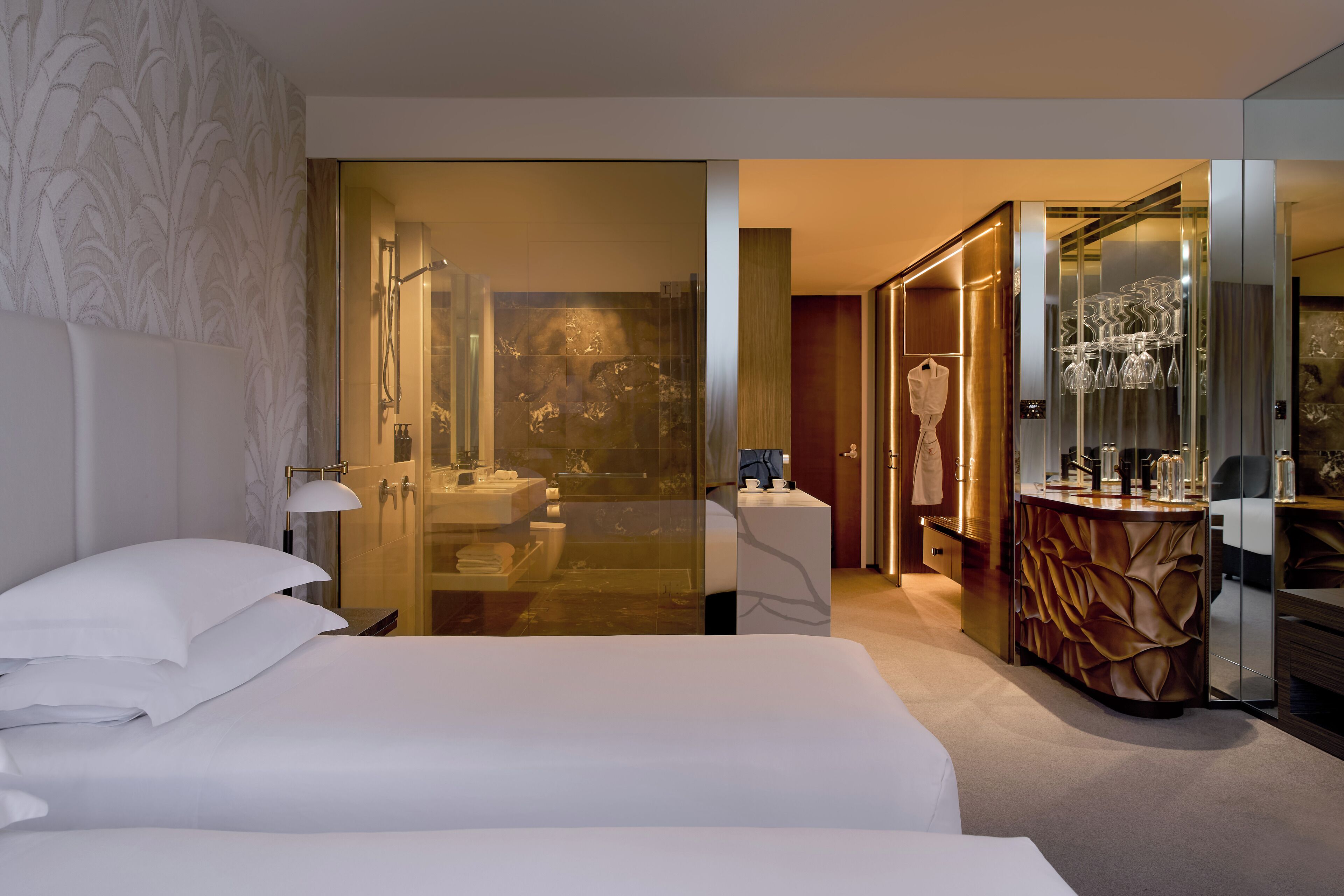 A hotel room with a large bed, a bathroom with a glass shower enclosure, and a vanity with a mirror.