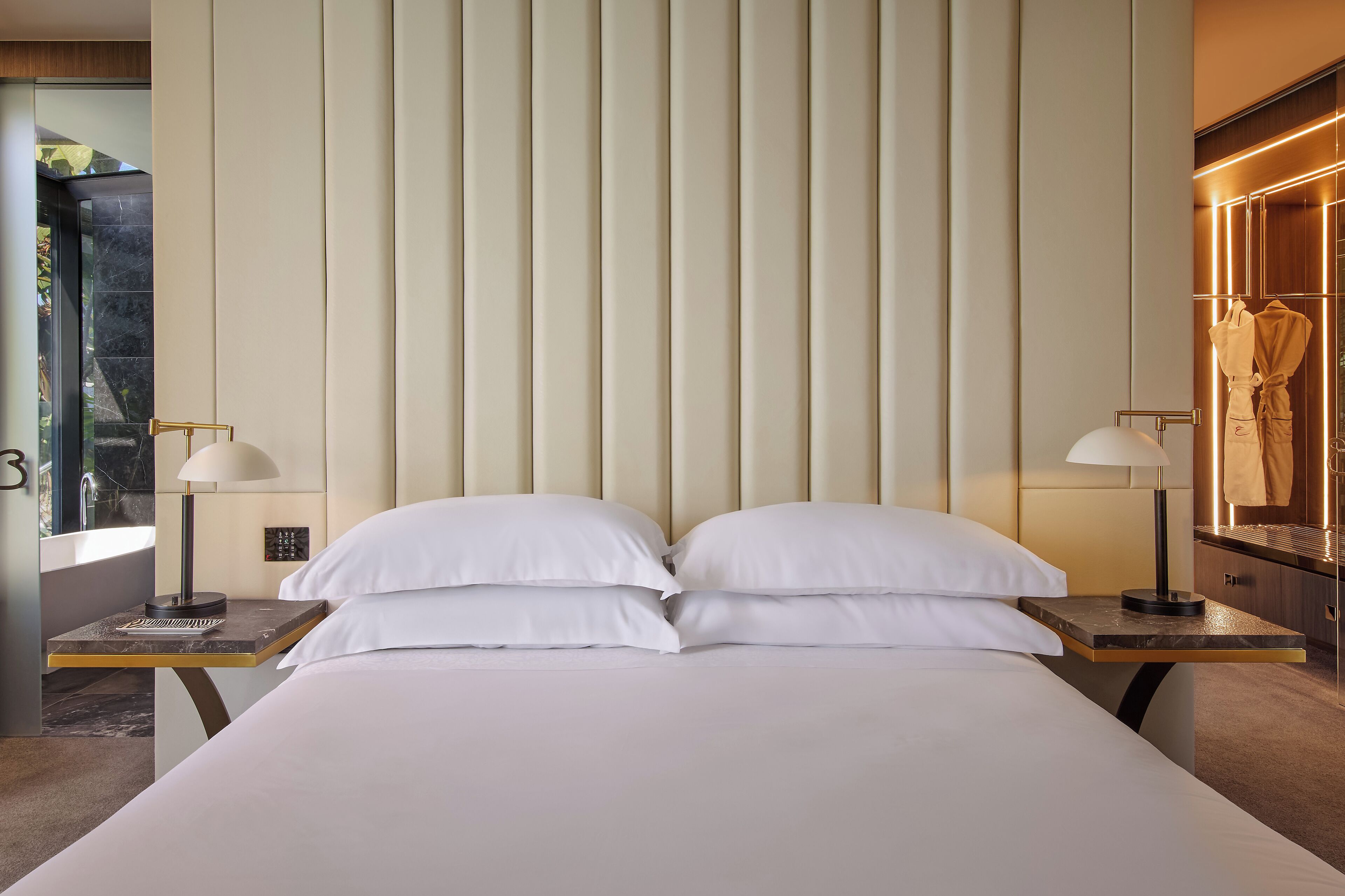 A hotel room with a large bed, two bedside tables with lamps, a vanity with a mirror, and a view of a balcony.