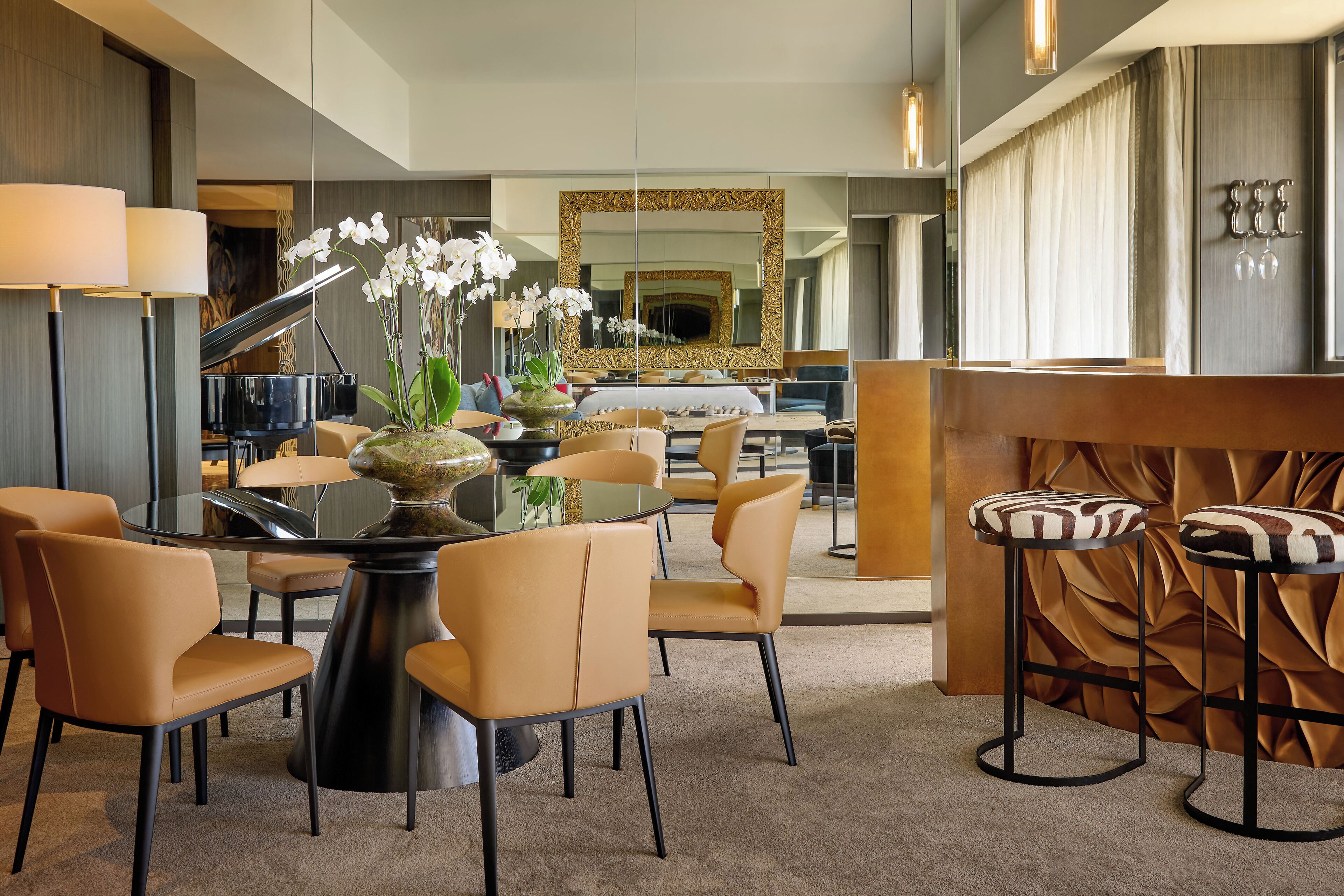 A modern hotel lobby with a round dining table, comfortable seating, a piano, and a large mirror.