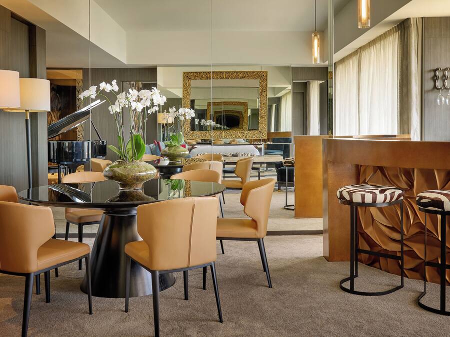 A modern hotel lobby with a round dining table, comfortable seating, a piano, and a large mirror.