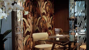Un comedor moderno con una mesa de vidrio, sillas blancas y un muro decorativo con un diseño de hojas.