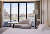 A hotel room with a large window, a bed, a round table, and a chair.