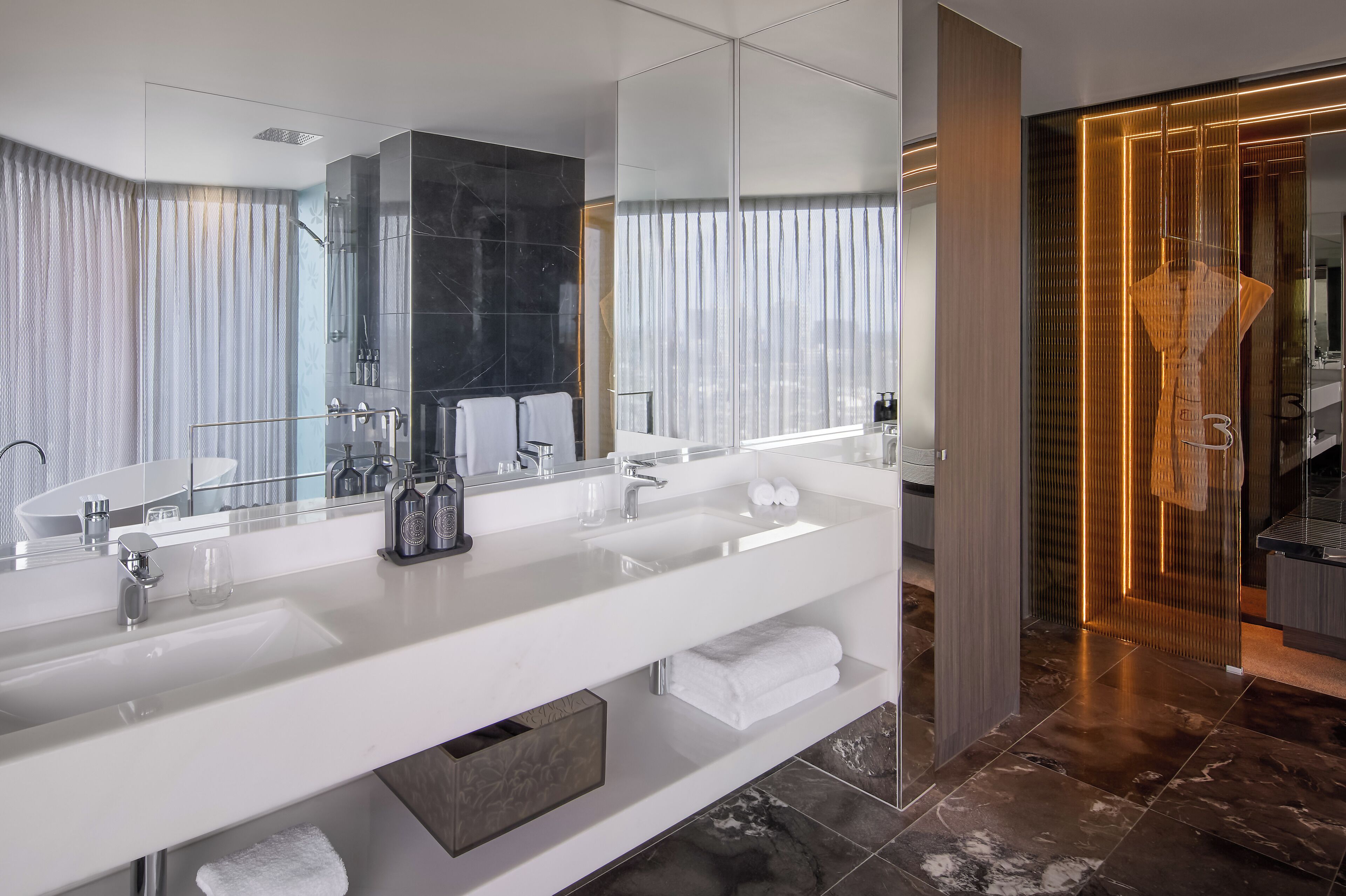Une salle de bain moderne avec un grand miroir, deux lavabos et une douche à l’italienne.