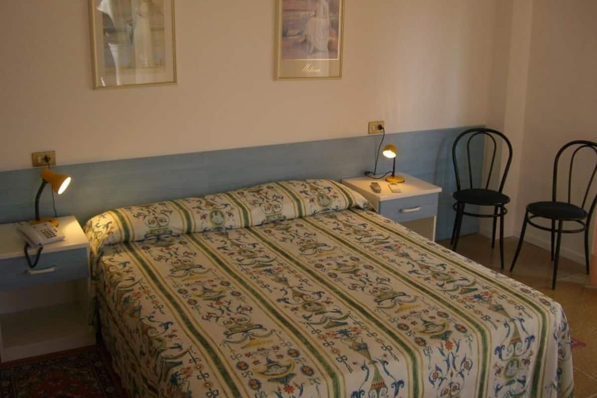 Un dormitorio con una cama, dos mesitas de noche, dos sillas y dos cuadros en la pared.