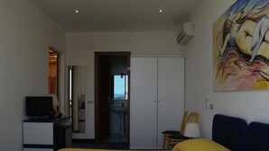 Habitación de hotel con cama, escritorio con televisor, armario y baño visible a través de una puerta abierta.