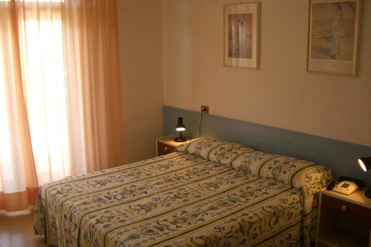 Un dormitorio con una cama, una mesita de noche, una lámpara y un cuadro en la pared.
