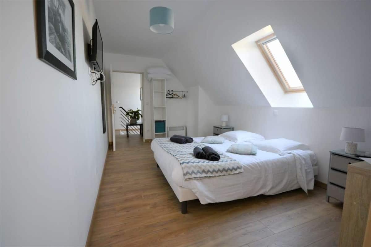 A bedroom with a skylight, a bed with pillows, a bedside table, and a wardrobe.
