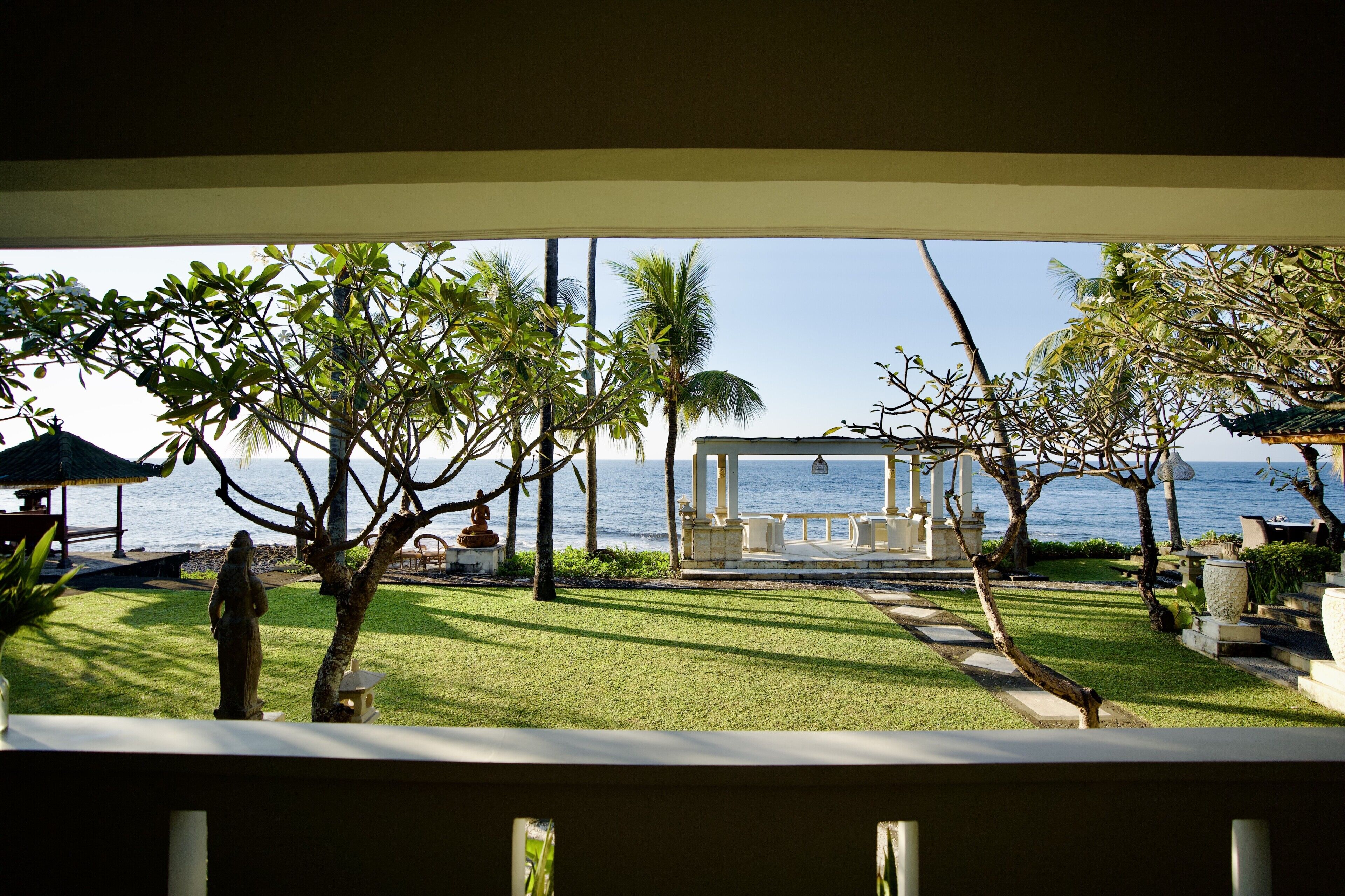 Vista de un patio frente al mar con un quiosco, palmeras y una estatua.