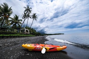 A kayak on a pebbly beach with palm trees and a house in the background. - Poinciana Resort Bali (Tejakula)