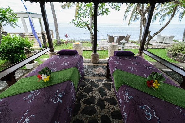 Two massage beds with green towels and flowers, a stone-tiled floor, and a view of the sea. - Poinciana Resort Bali (Tejakula)