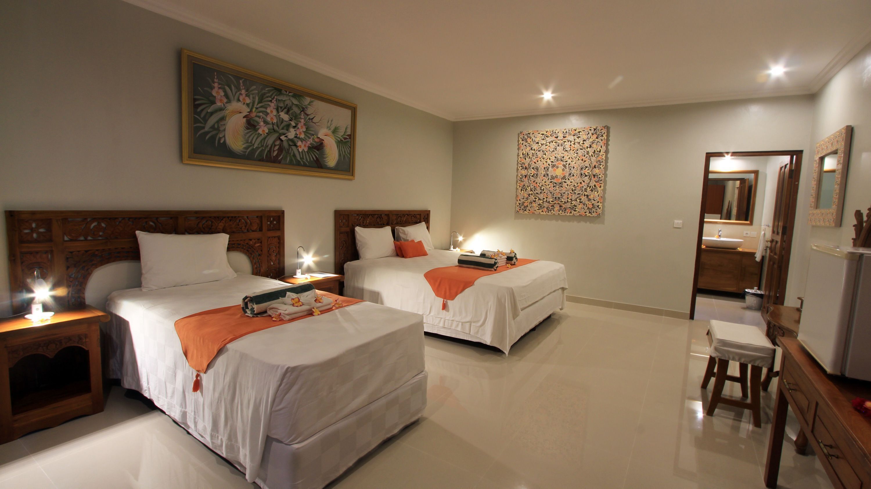 A hotel room with two beds, a desk, a chair, a mirror, and artwork on the walls.