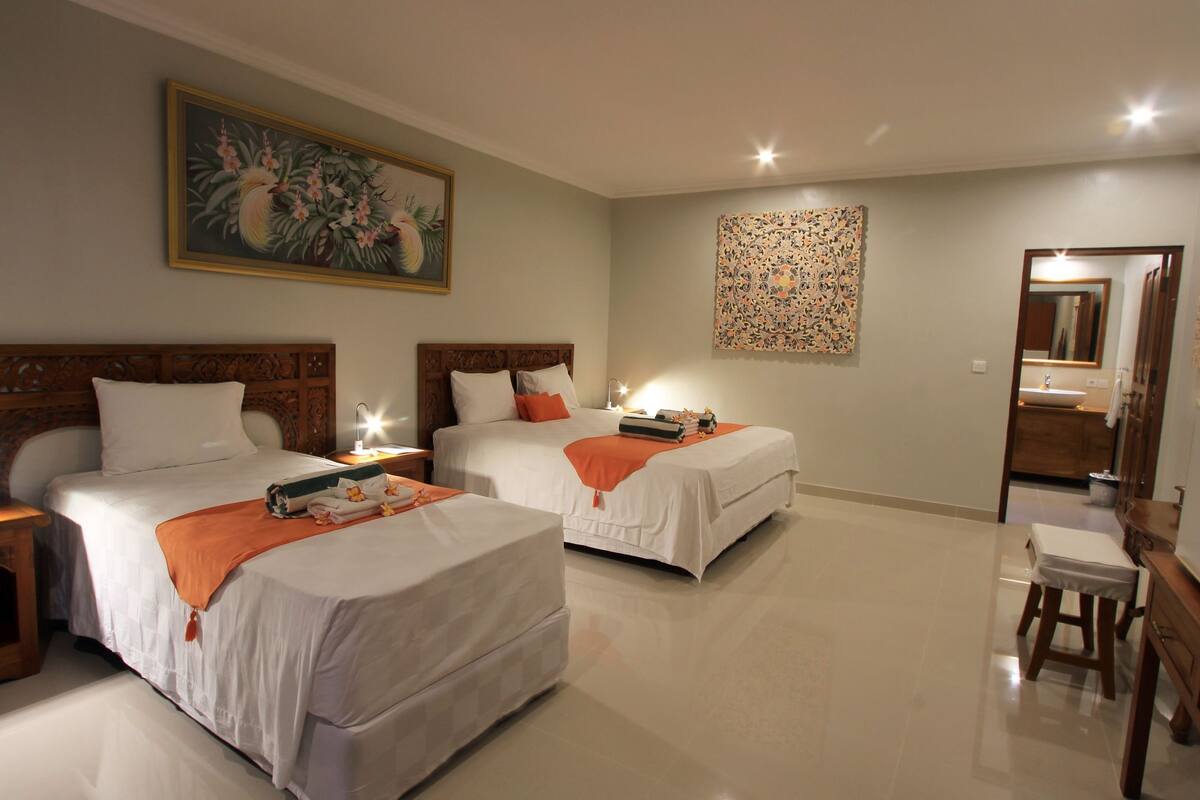 A hotel room with two beds, a desk, a chair, a mirror, and artwork on the walls.
