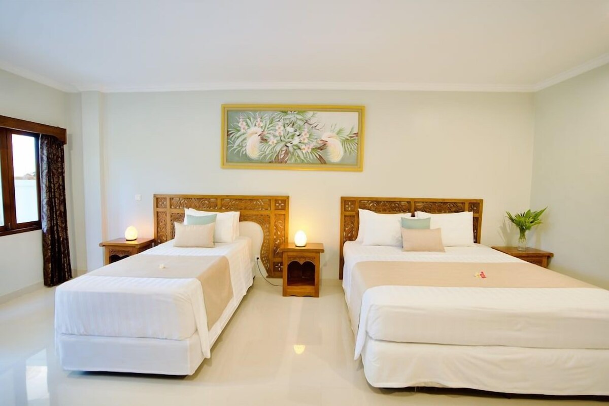 A hotel room with two beds, a painting above the beds, and a window with curtains.