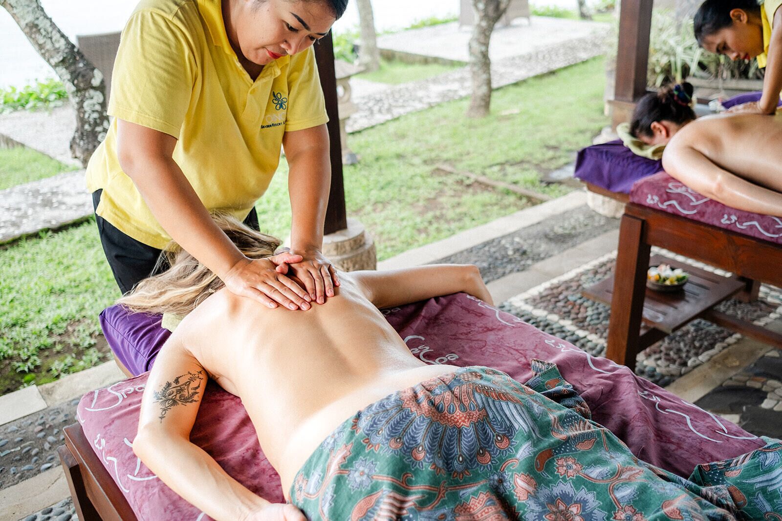 En massagebehandling utomhus, på en plats med en stenlagd gång och omgivande grönska.