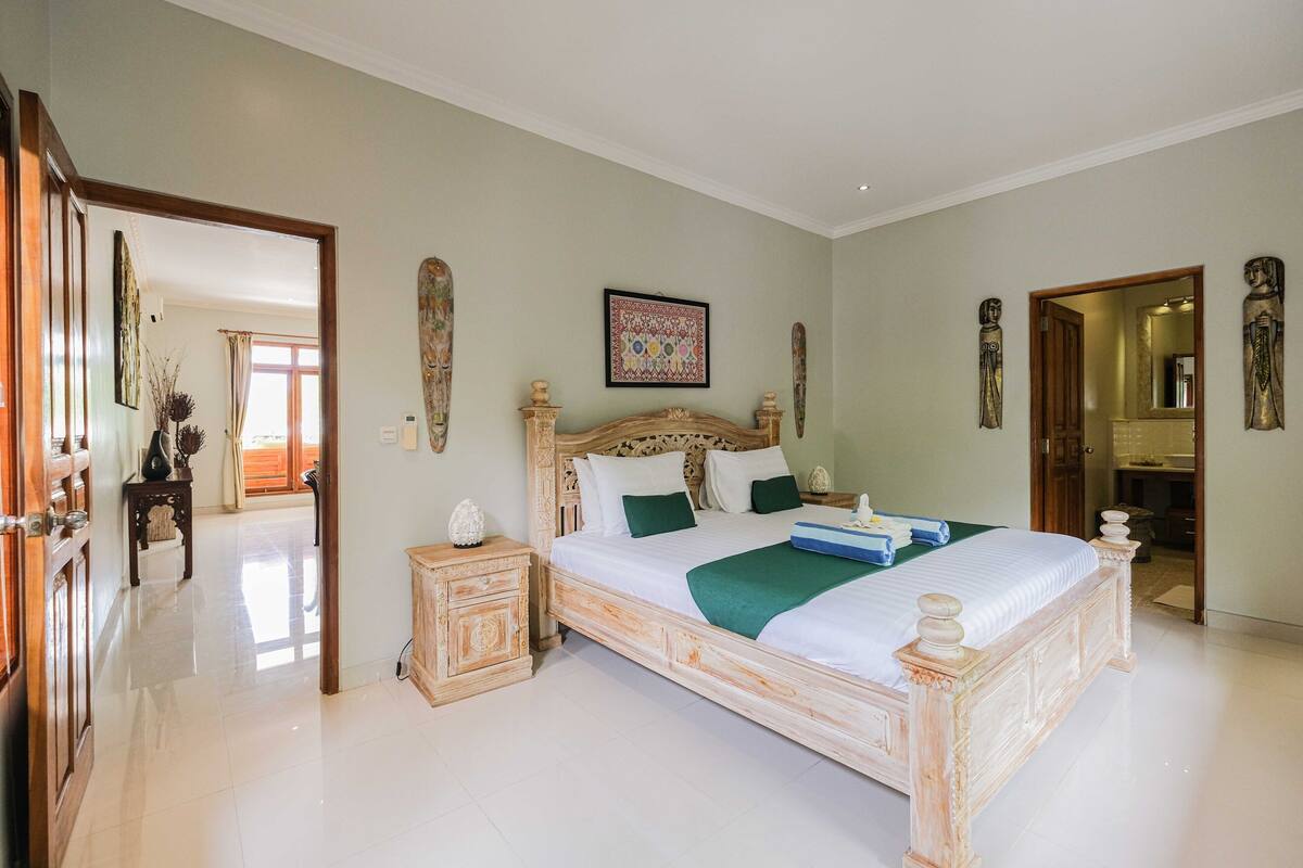 A spacious bedroom with a large bed, wooden headboard, and a green throw blanket.