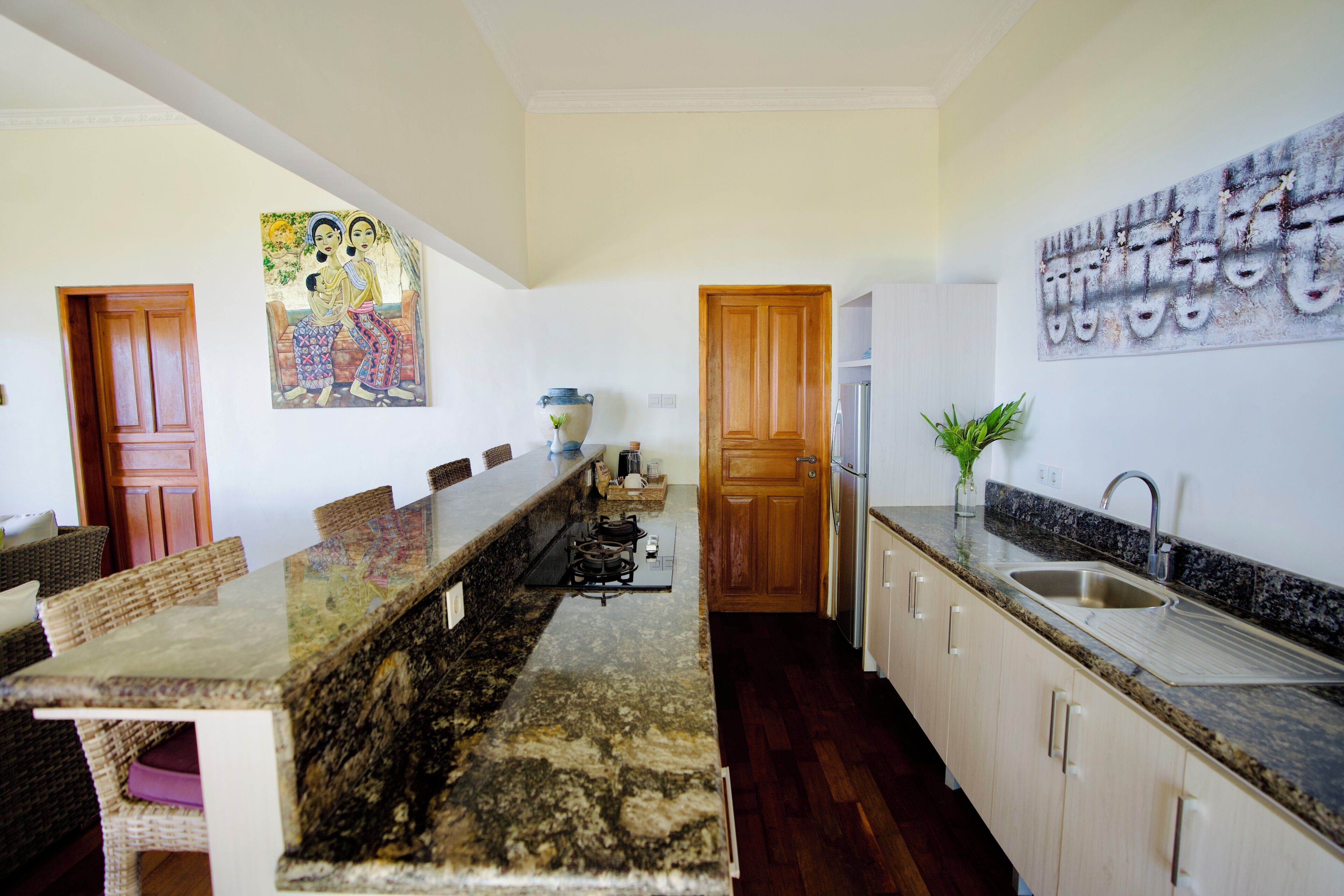 A kitchen with a long island, wooden cabinets, a sink, and a painting on the wall.