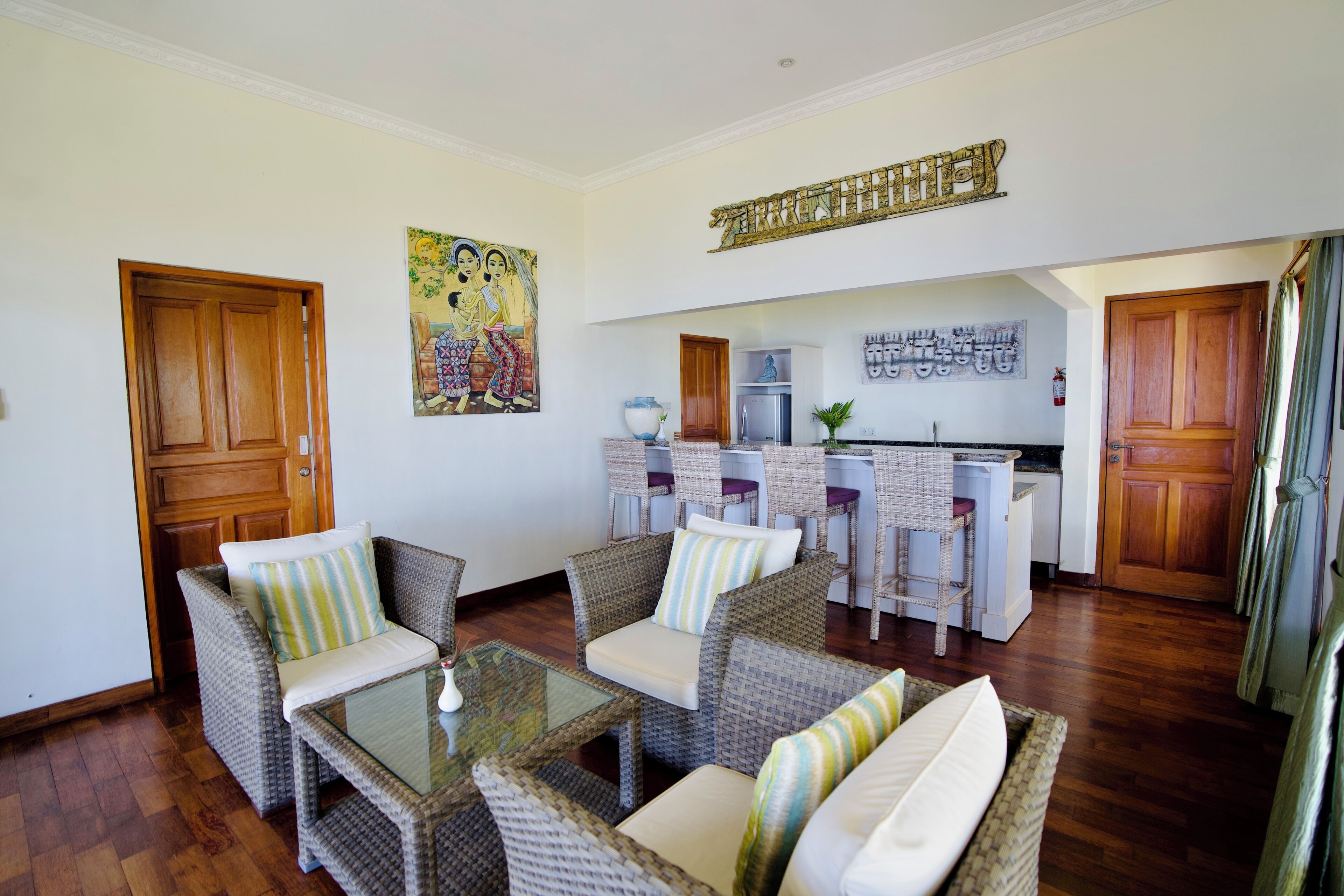A living room with wicker furniture, a glass coffee table, and a kitchen in the background.