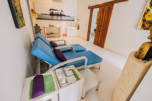 A living room with a blue sofa set, a small white table with a tray, and a wooden door. - Poinciana Resort Bali (Tejakula)