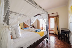 A four-poster bed with a canopy, a wooden desk, and a view of the outdoors through a window. - Poinciana Resort Bali (Tejakula)