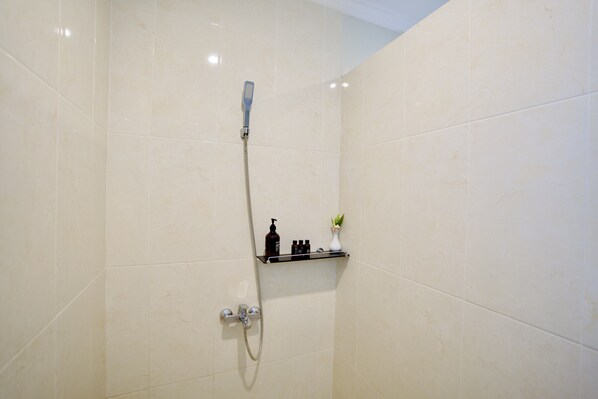 A shower with a handheld showerhead, a wall-mounted faucet, and a shelf with toiletries.