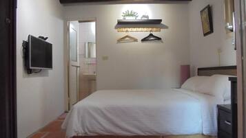 A bedroom with a bed, a television mounted on the wall, and a shelf with decorative items.
