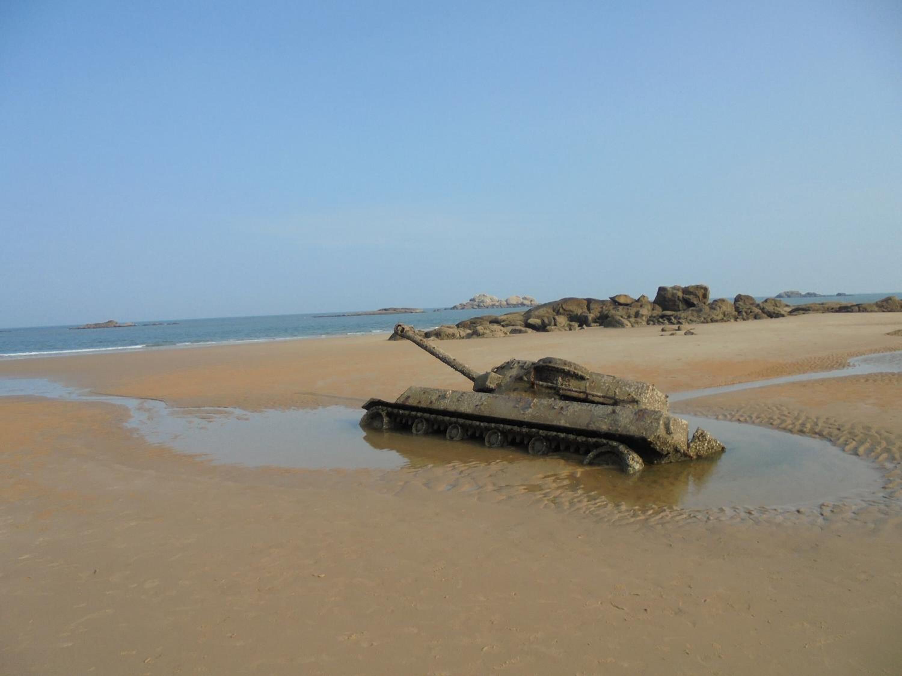 Un tanque en una playa arenosa con afloramientos rocosos al fondo.