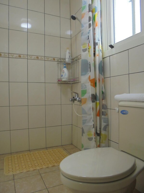 A small bathroom with a toilet, a shower with a curtain, and a shelf with toiletries.