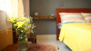 Une chambre à coucher avec un lit, une table de chevet et un vase rempli de fleurs jaunes, posé sur un tabouret en bois.