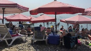 A beach with multiple red and white striped umbrellas, lounge chairs, and people swimming in the water. - Pinar Kir Evi (Arhavi)