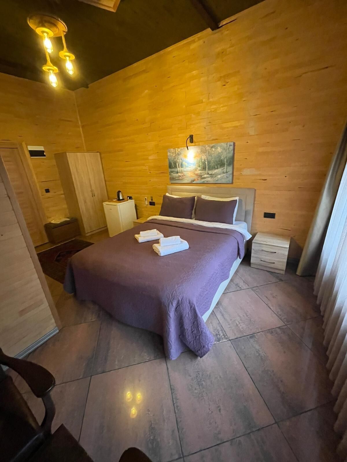 Een slaapkamer met een groot bed, houten wanden, een schilderij en een nachtkastje.