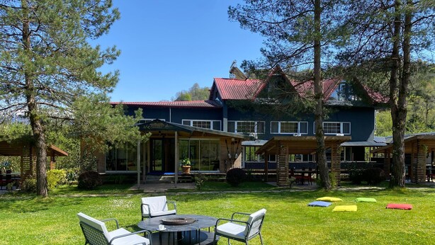 A large house with a red roof, a covered patio, and a grassy lawn with outdoor furniture. - Pinar Kir Evi (Arhavi)