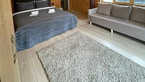 A bedroom with a bed, a sofa, a rug, wooden walls, and a ceiling light. - Pinar Kir Evi (Arhavi)