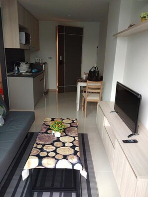 A compact living space with a kitchenette, a sofa, a dining table with a decorative centerpiece, a TV, and a chair.