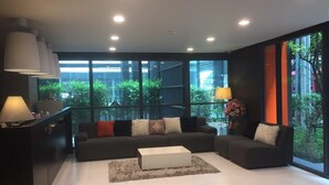 A modern living room with a sectional sofa, a coffee table, and a large window offering a view of greenery. - Apartment at Punnawithi BTS (Bangkok)
