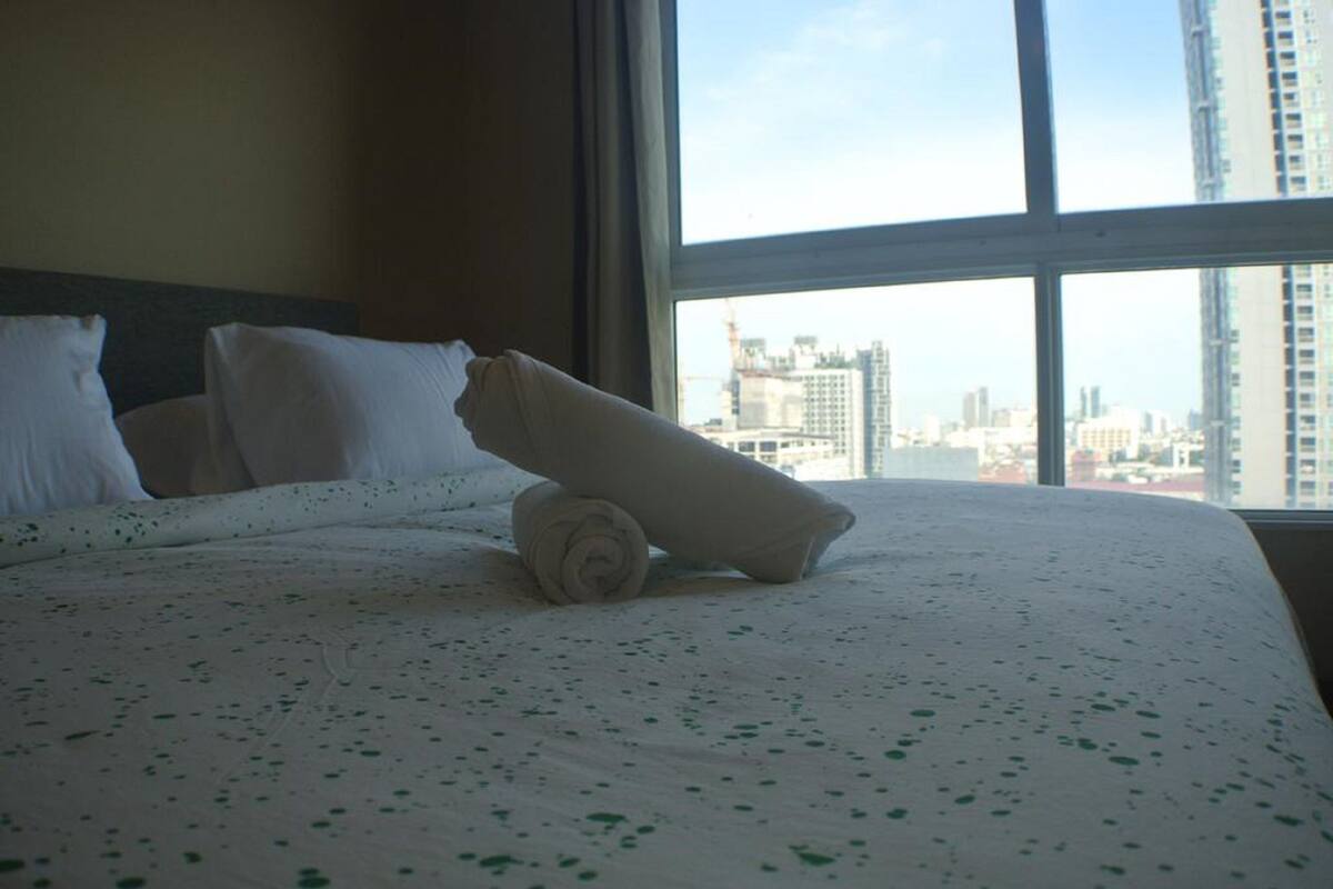A hotel room with a large window, a neatly made bed with white linens, and a cityscape view.
