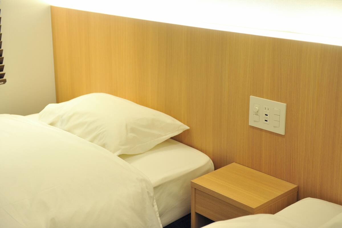 A hotel room with a bed, a wooden nightstand, and a wall socket.