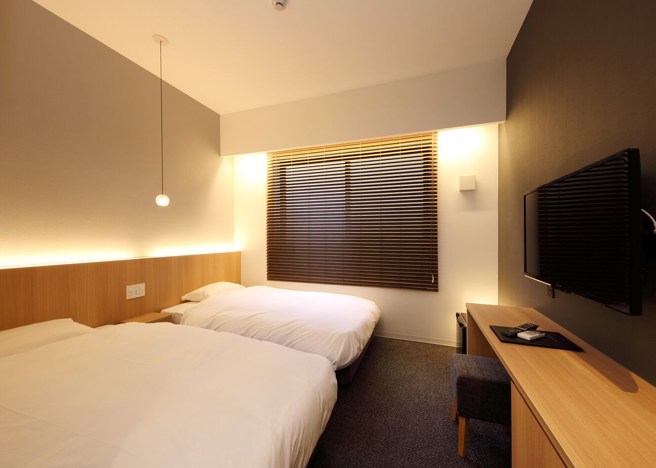 A hotel room with two beds, a desk, a television, and a window with blinds.