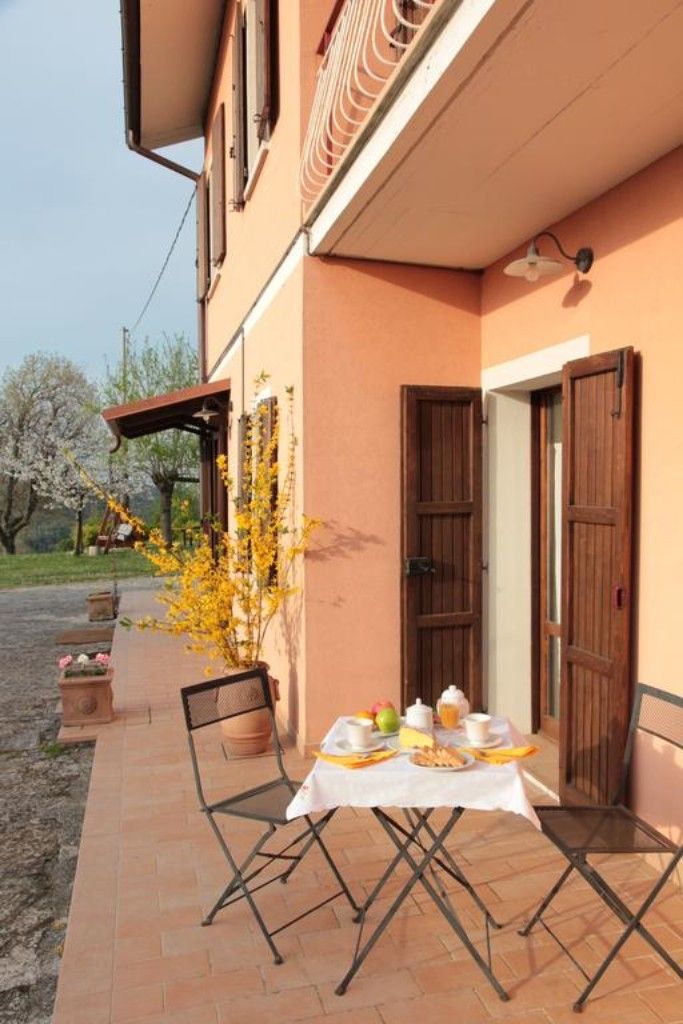 Un patio con mesa lista para el desayuno, asientos al aire libre y vistas a un jardín con árboles en flor.