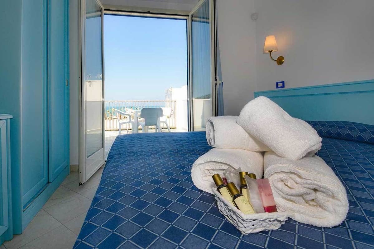 A hotel room with a large bed, a basket of towels, and toiletries.