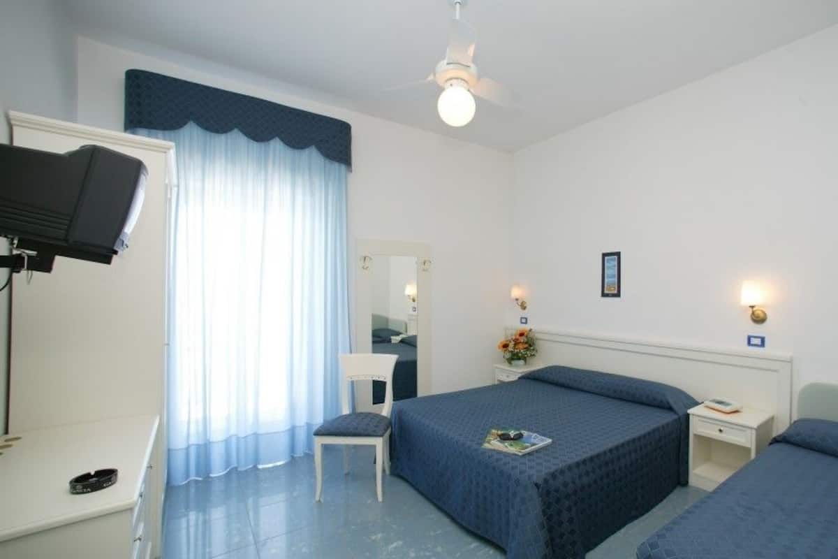 A hotel room with a bed, bedside tables, a desk, a chair, a television, and a window with curtains.