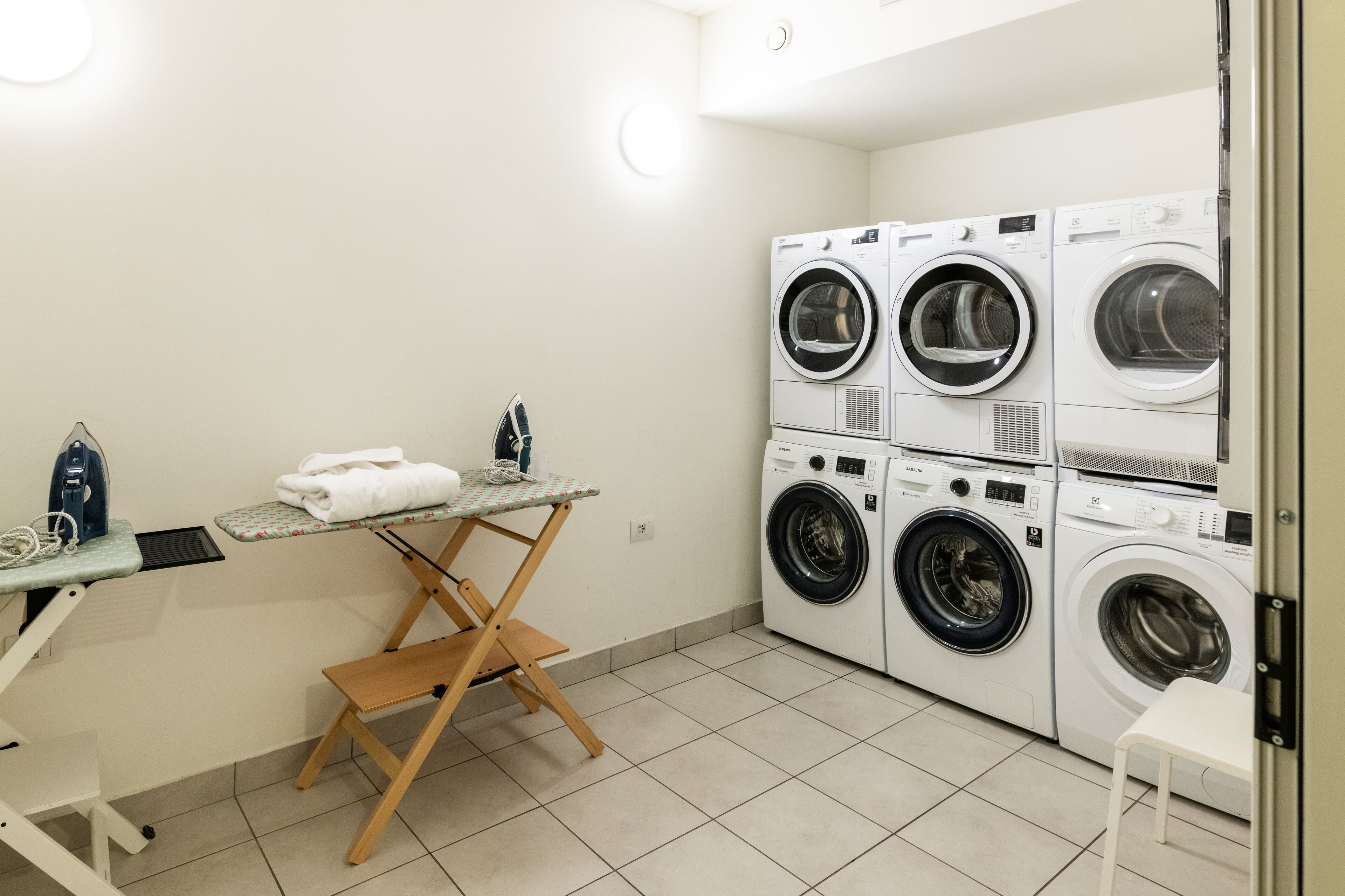 A laundry room with a folding table, ironing board, and stacked washing machines.