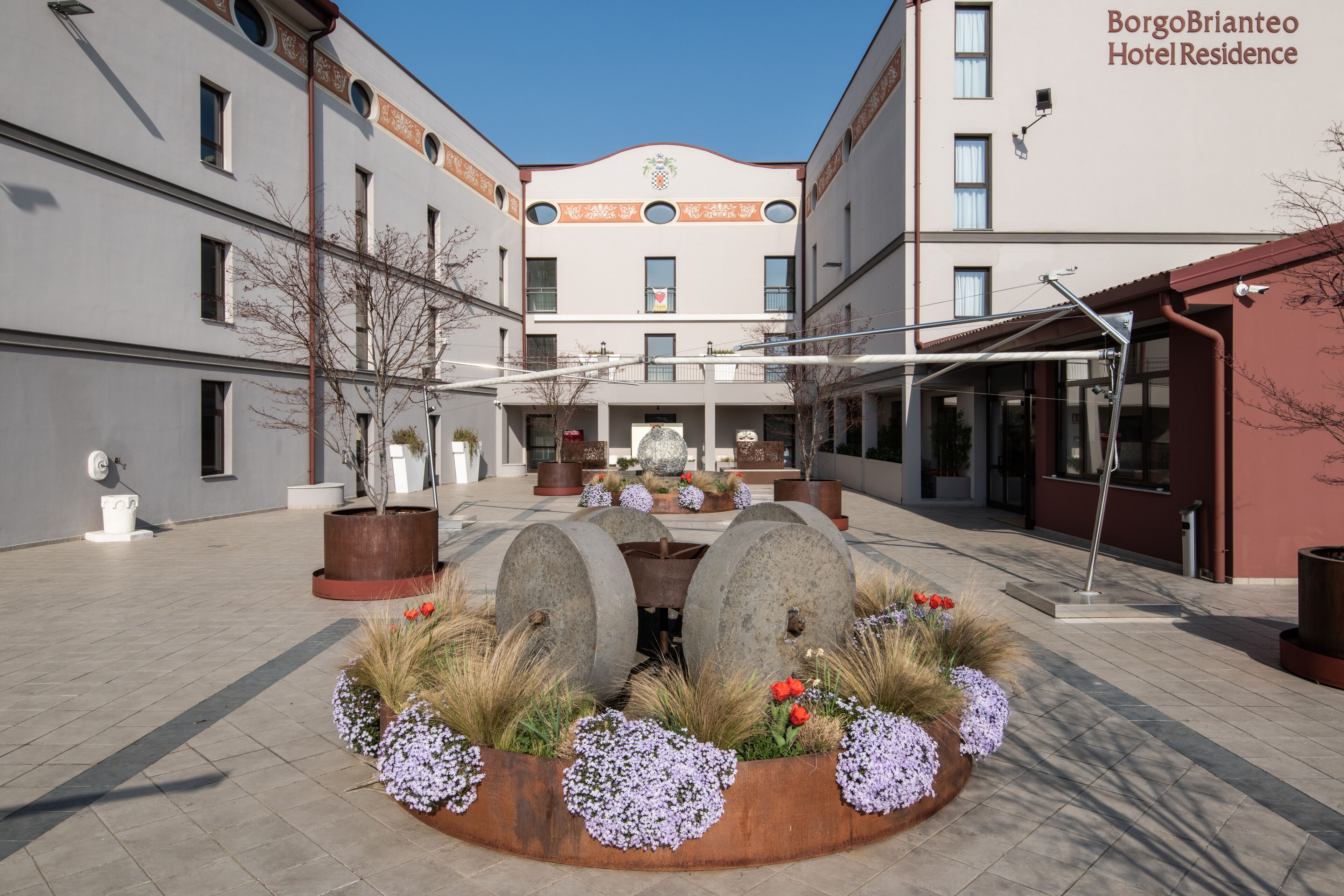 A courtyard with a central fountain, surrounded by flower beds and potted plants.
