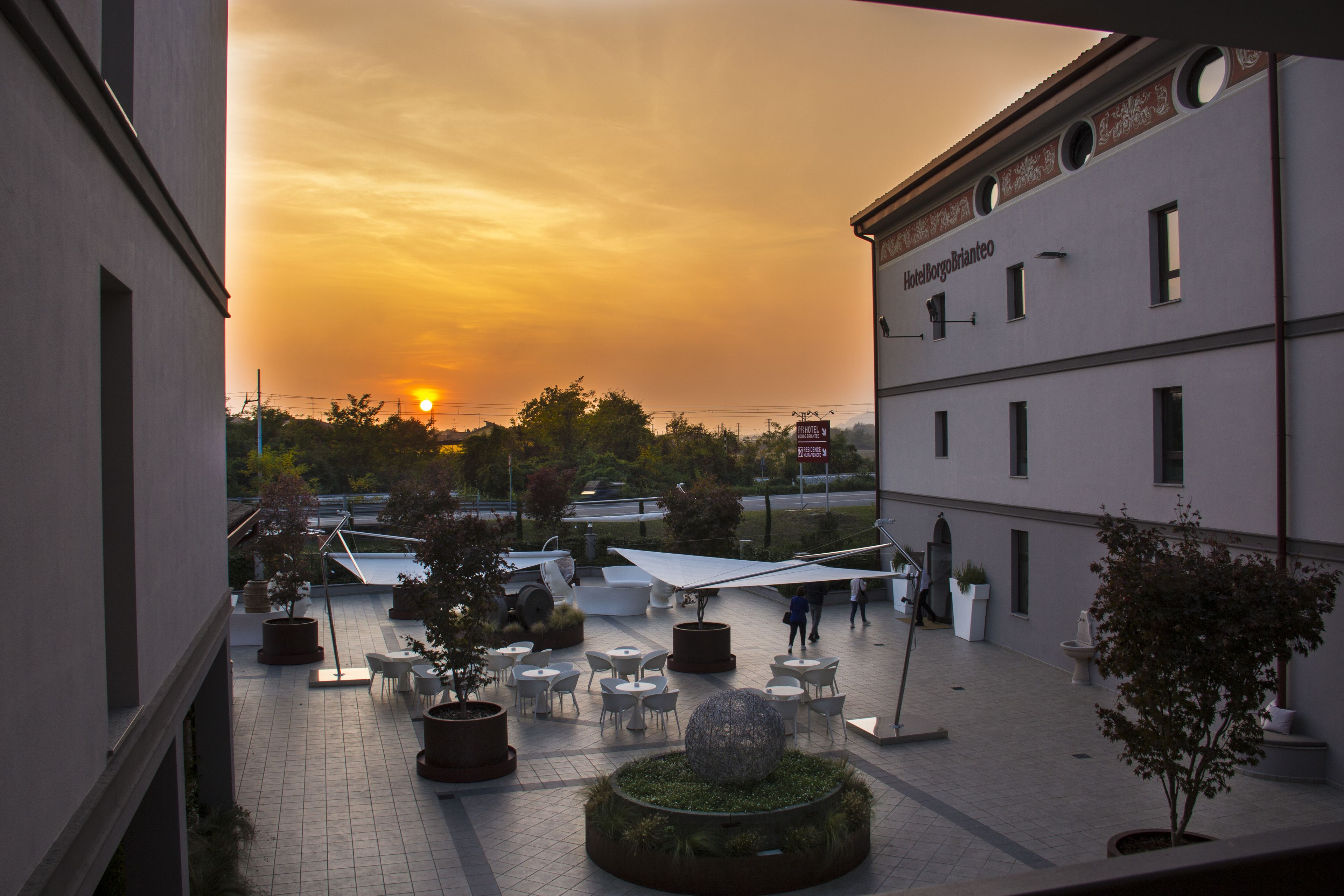 A hotel courtyard with outdoor seating, a large decorative sphere, and a sunset in the background.