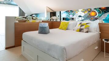 A modern hotel room with a large bed, a bedside table, a mirror, and a colorful abstract painting on the wall.