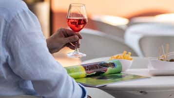 A person sitting at an outdoor table with a glass of red wine, a menu, and a bowl of fries.