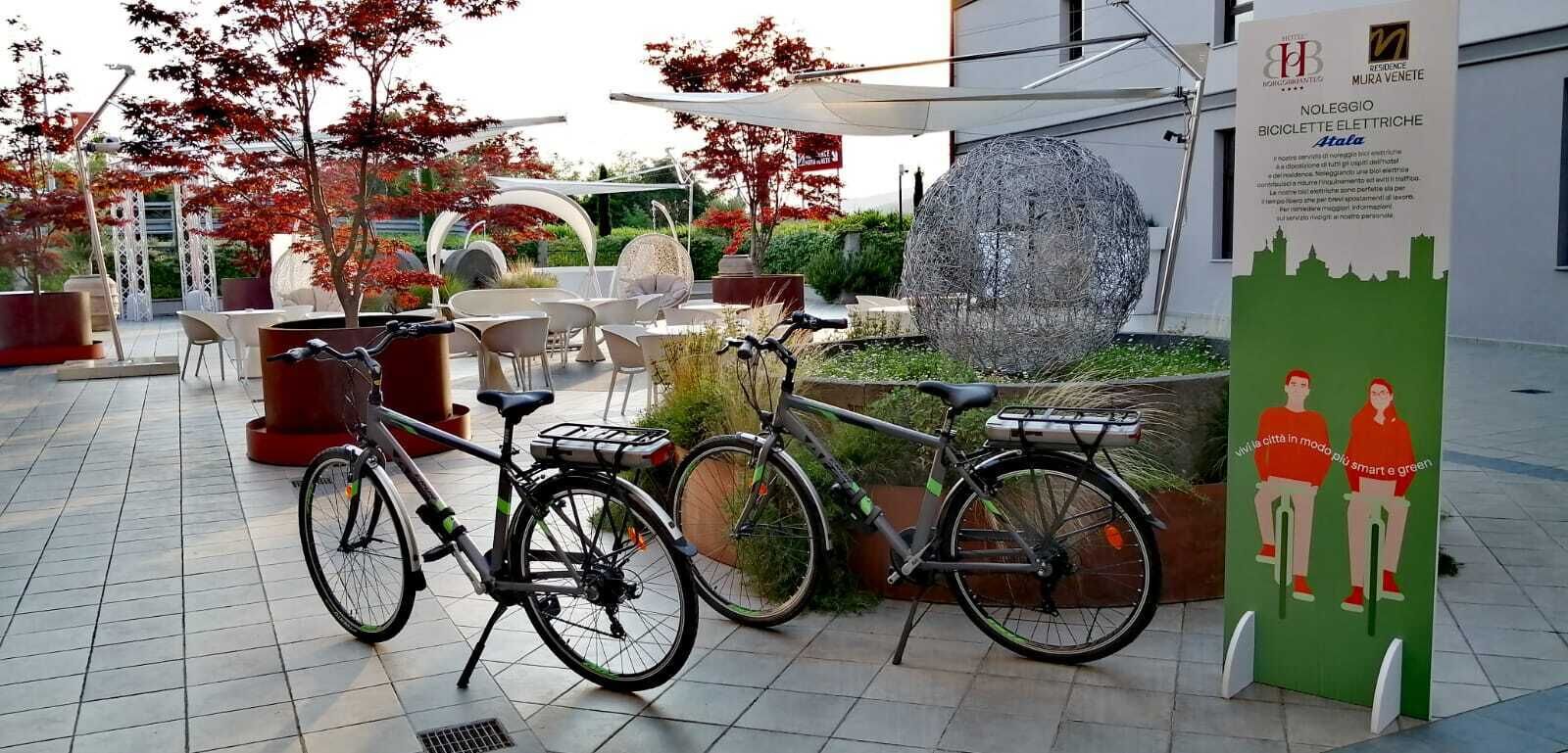 A bicycle parked in an outdoor seating area with a fountain, surrounded by red-leaved trees and modern chairs.
