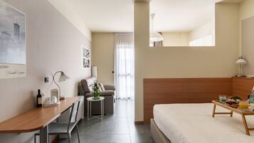 A hotel room with a bed, a desk, a chair, a small table with a tray of breakfast, a lamp, and a window with curtains.