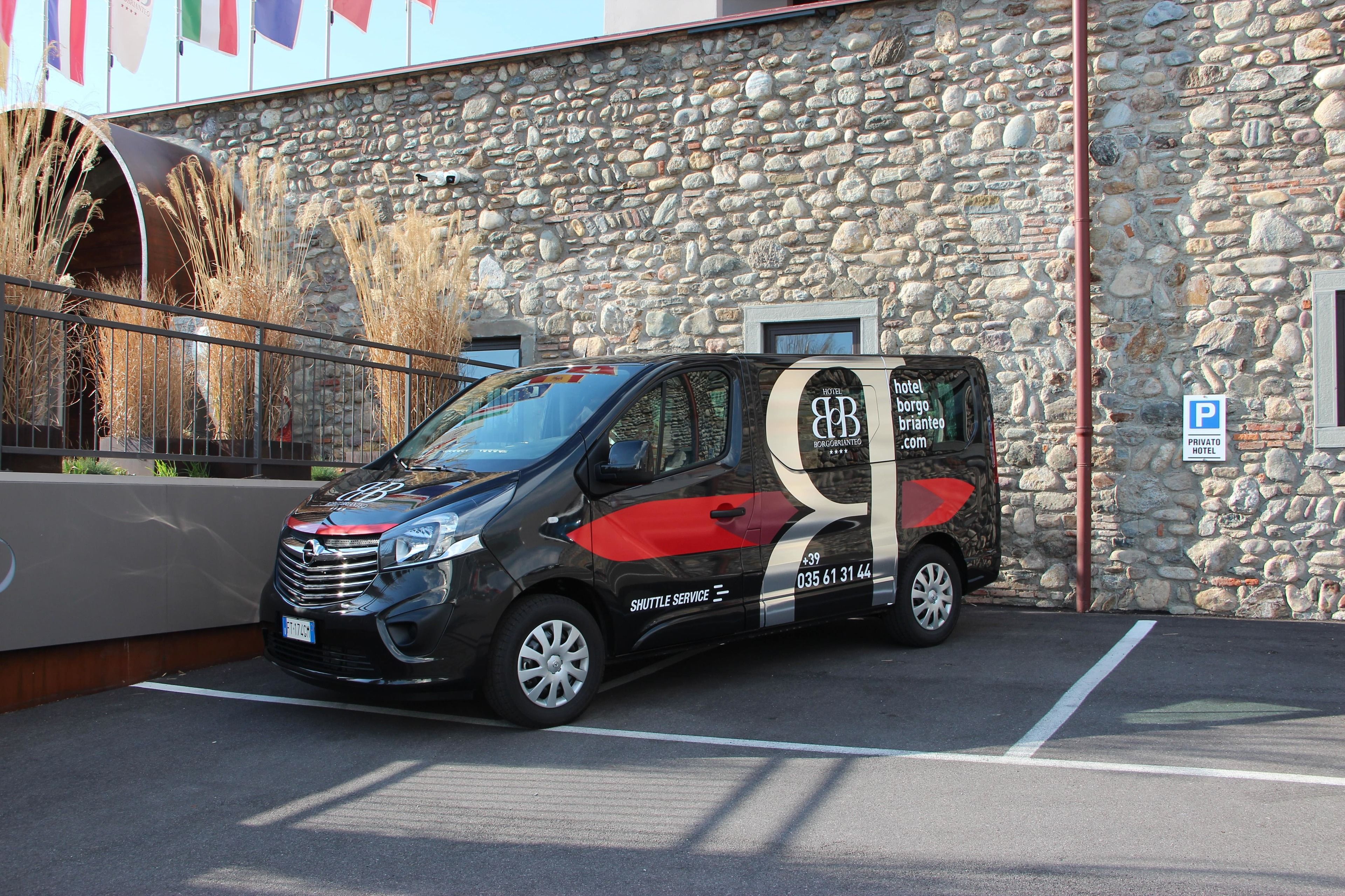 A shuttle service vehicle parked in front of a stone building with a sign indicating a private parking area.