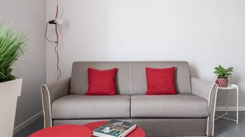 A modern living room with a grey sofa, red cushions, a red coffee table, and a potted plant.