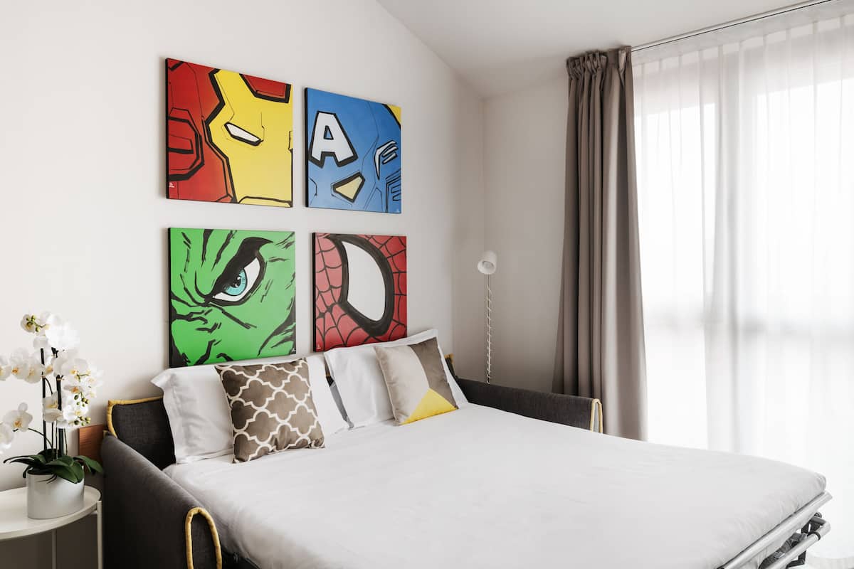 Un dormitorio moderno con cama, mesita de noche, lámpara y cuadros en la pared.